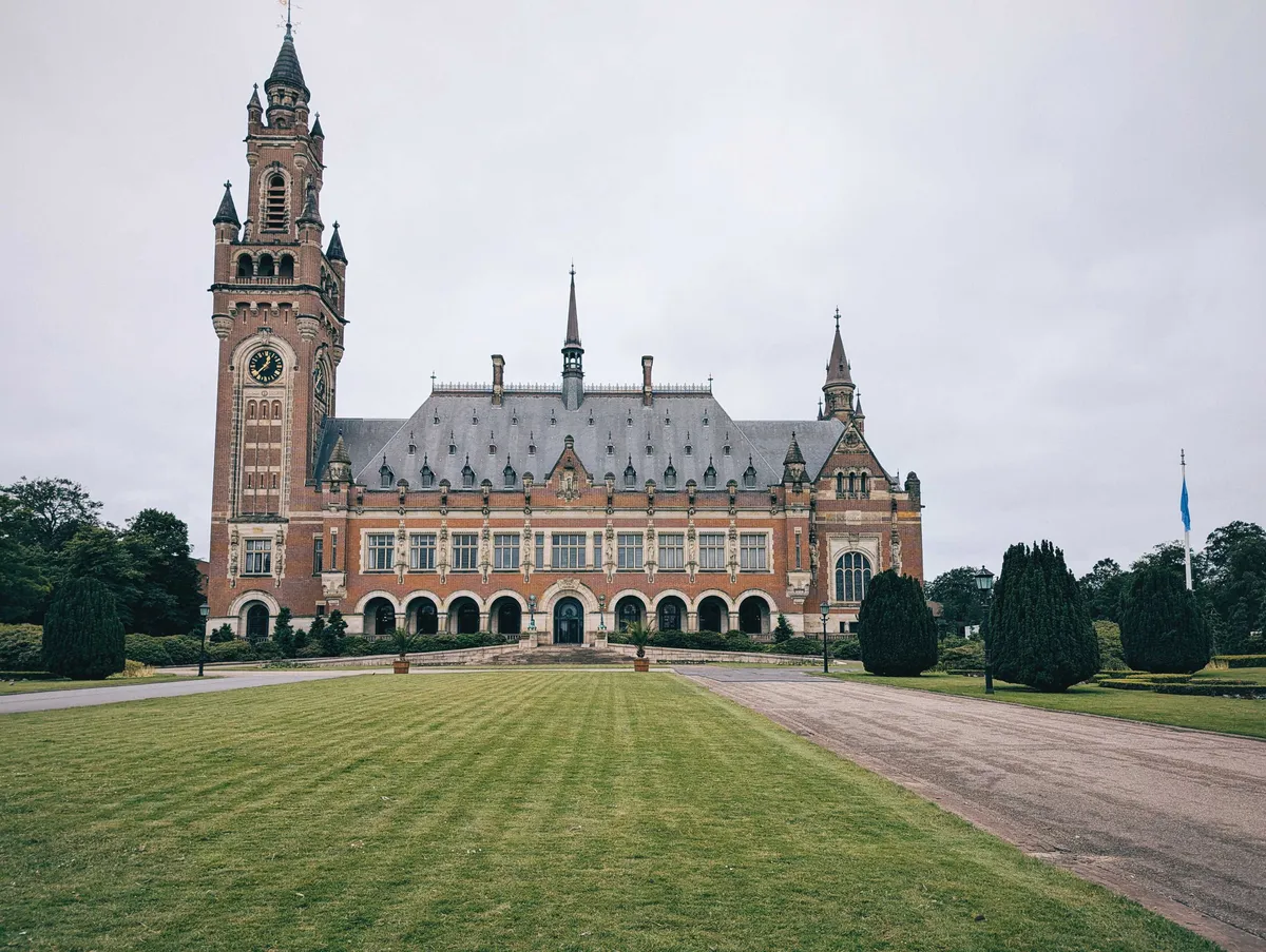 The front of the Peace Palace, featuring Neo-Renaissance style and incorporating Gothic and Byzantine influences. There is a sprawling green lawn and some shrubbery.