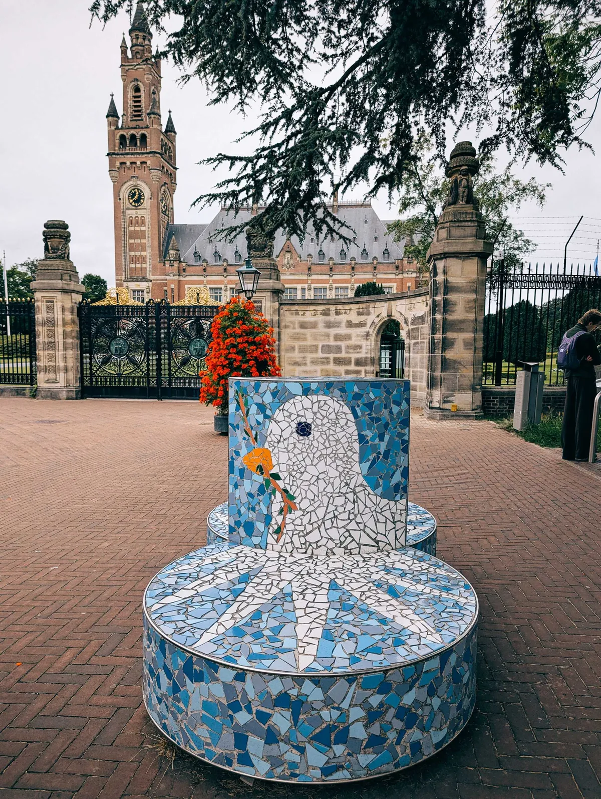 A bench outside of the Peace Palace gates made out of mosaic tiles. It shows a dove holding an olive branch against a blue background.