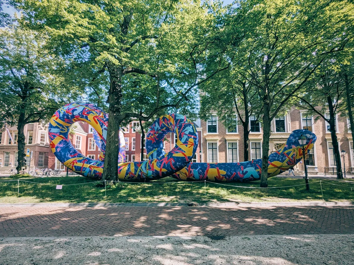 A giant, spiral snake-like inflatable sculpture with a colorful pattern sits on a grassy field in the park.