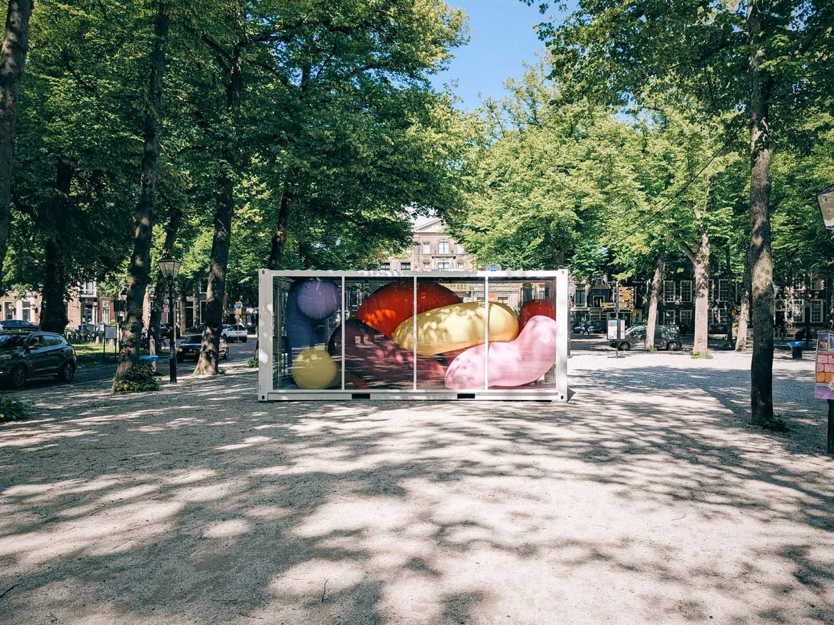 A large white container with transparent glass windows displays several large inflatable tube-like sculptures of varying colors inside.