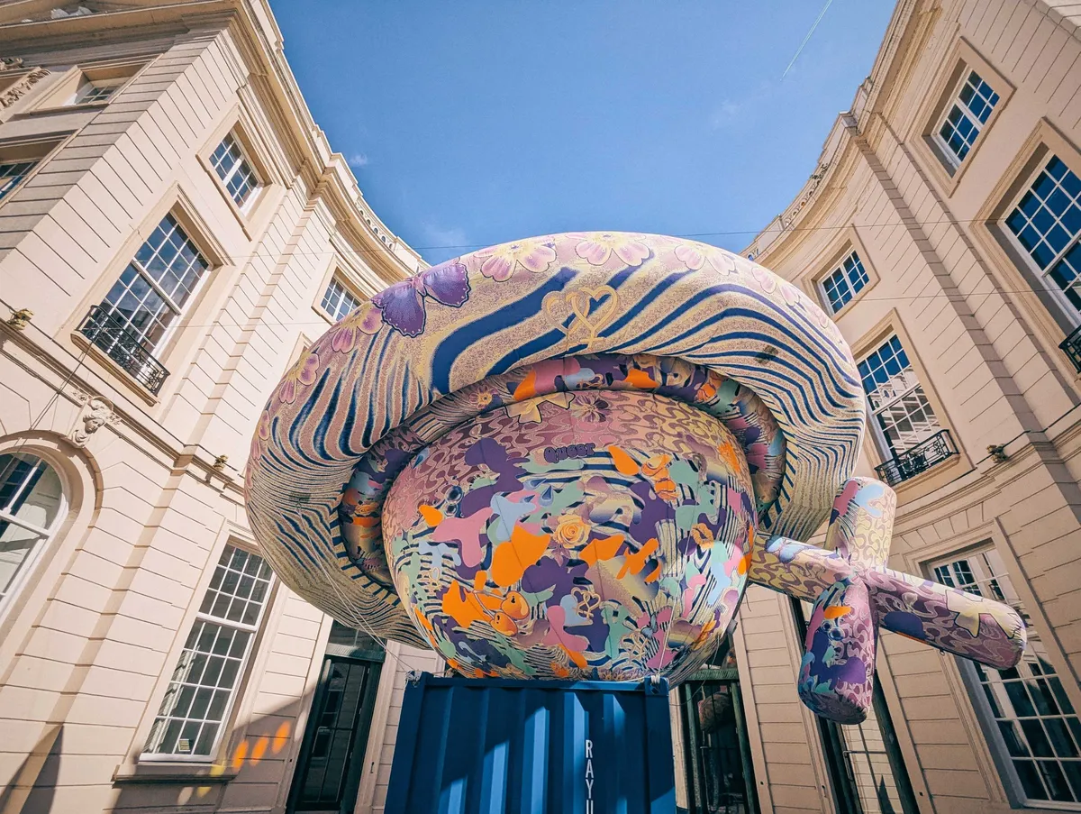 A massive inflatable UFO-shaped sculpture is placed on top of a blue container. It has psychedelic colors and patterns on the surface.