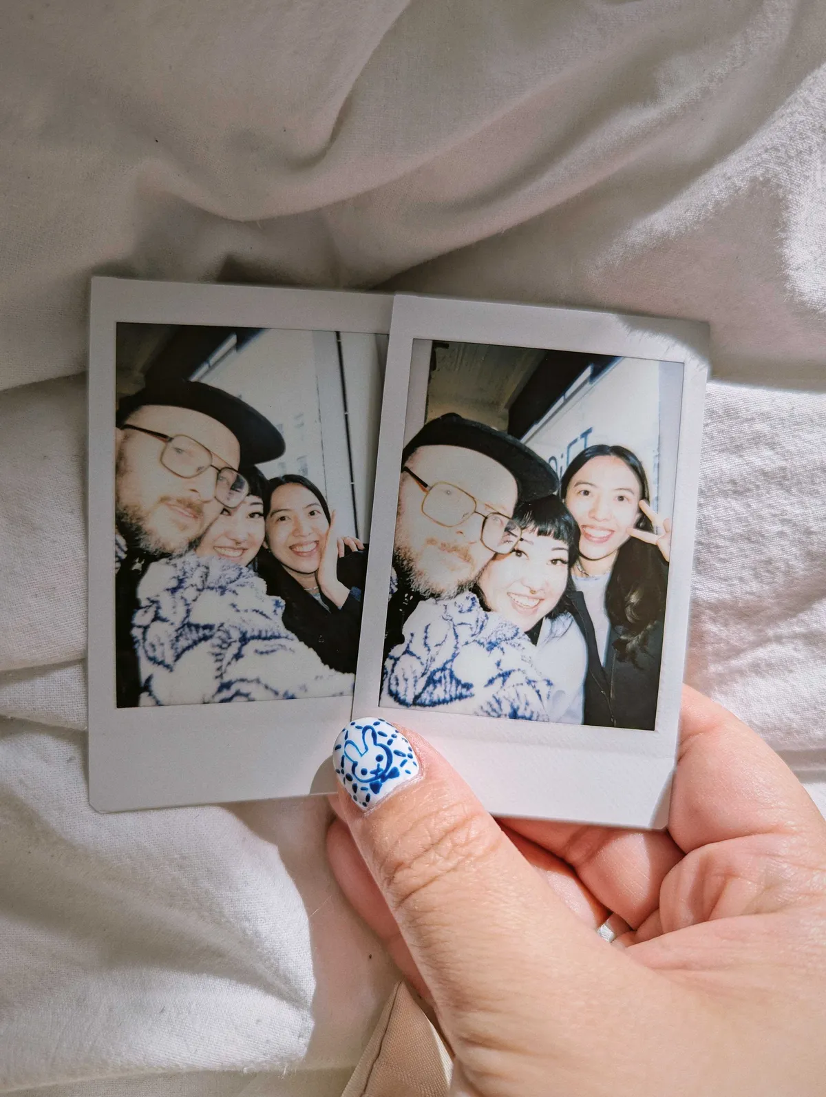 Peige holding two polaroids of nearly identical pictures of Daniel, Peige, and Han posing in a group selfie.
