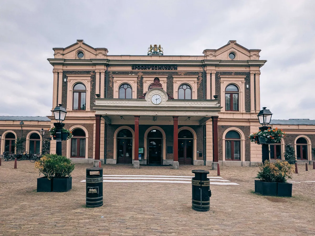 A neoclassical building with burgundy accents and a clock face on the portico.