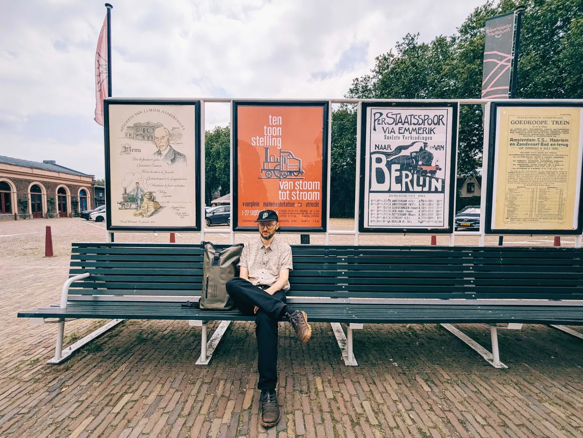 Daniel sitting on a green bench. A series of posters are behind him from various eras.