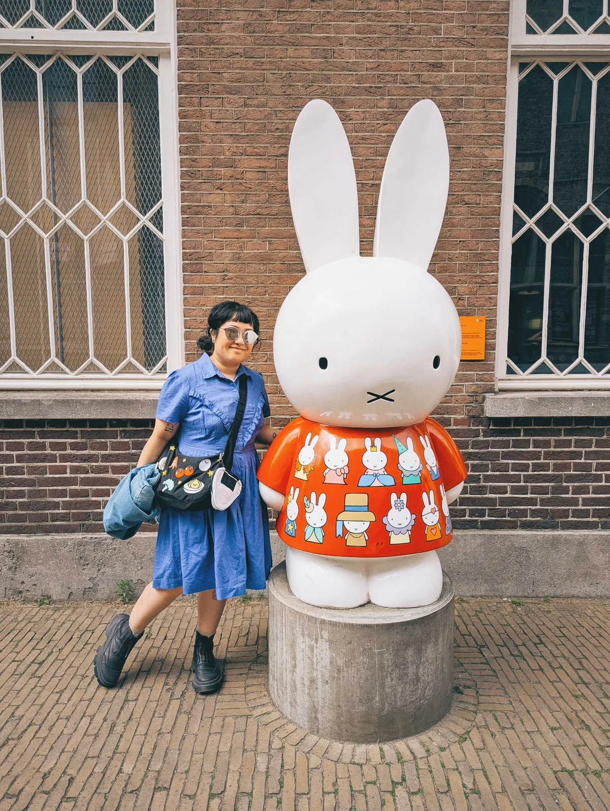 Peige wearing a blue dress and sunglasses poses next to the Miffy statue.