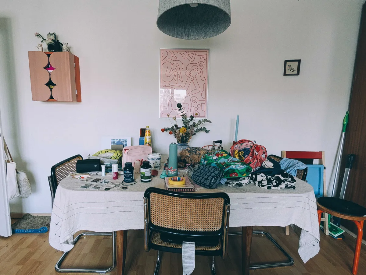 A dining table with piles of objects and clothes on the surface.