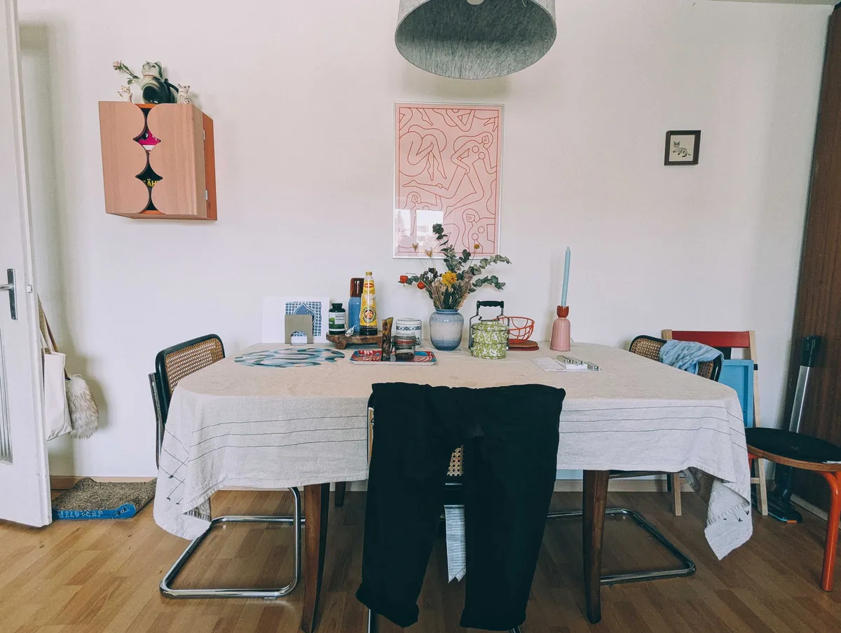 A dining table with a white linen table cloth. There are items still on it but ample space for dining.