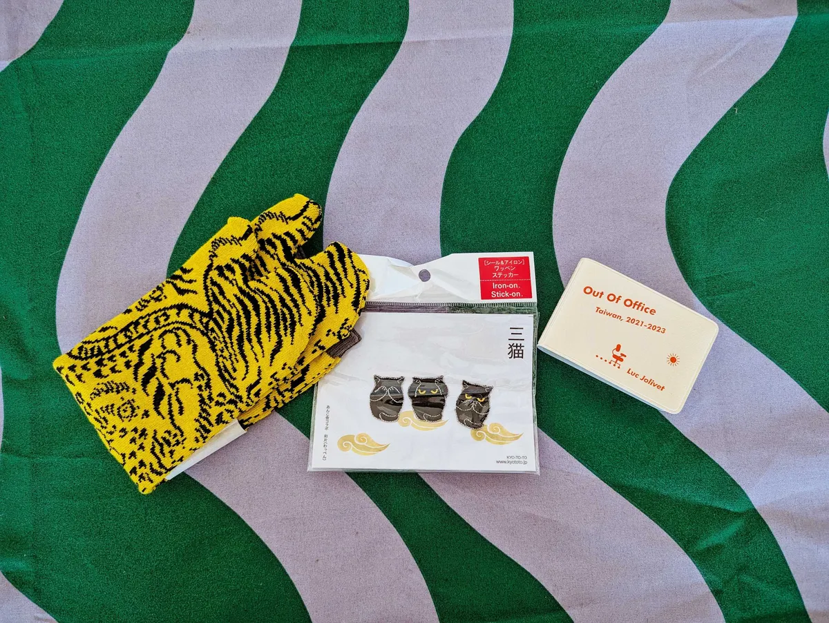 Yellow and black tiger print socks, three small black cats (see no evil, hear no evil, speak no evil), and a pocket-sized horizontal booklet with red type on the cover.