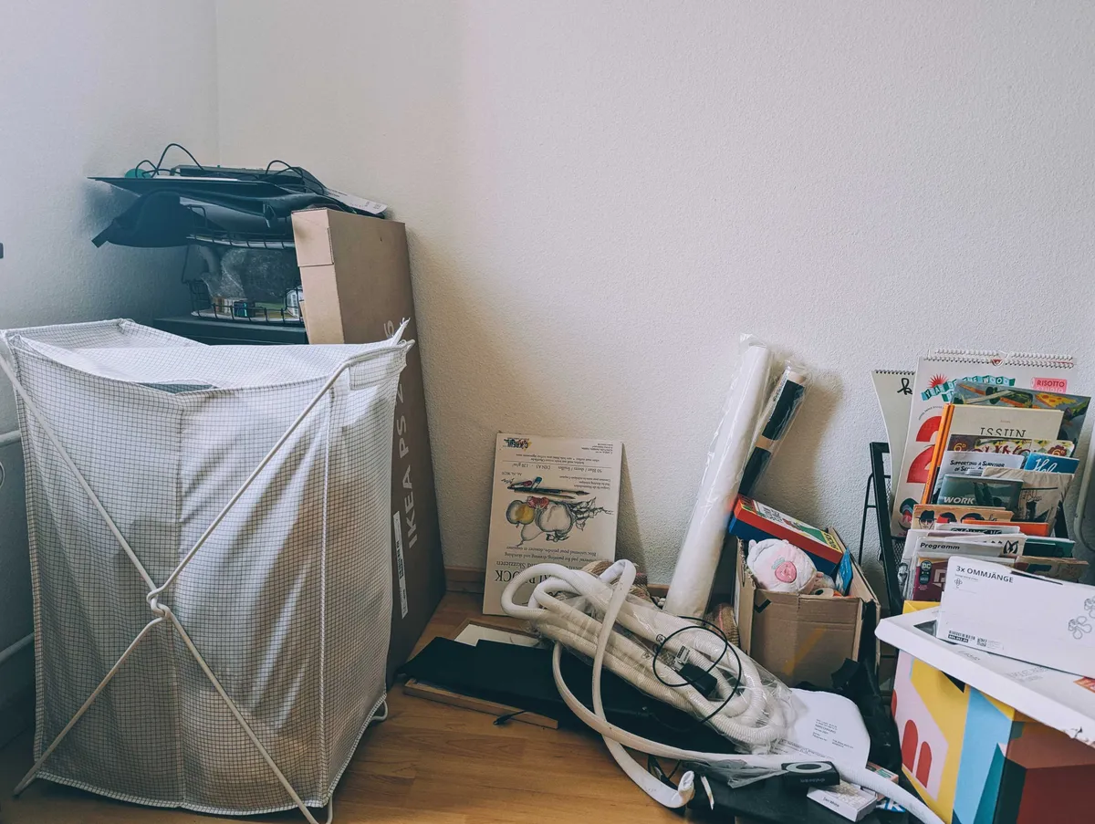A very messy corner, including a laundry hamper, unopened Ikea package, and lots of wires and tubes.