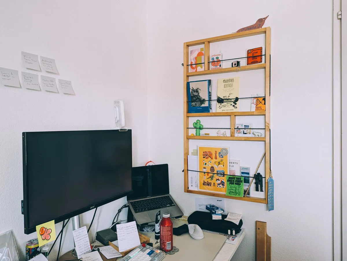 A wooden wall shelf with cords running through. It's been decorated with an assortment of trinkets and zines.