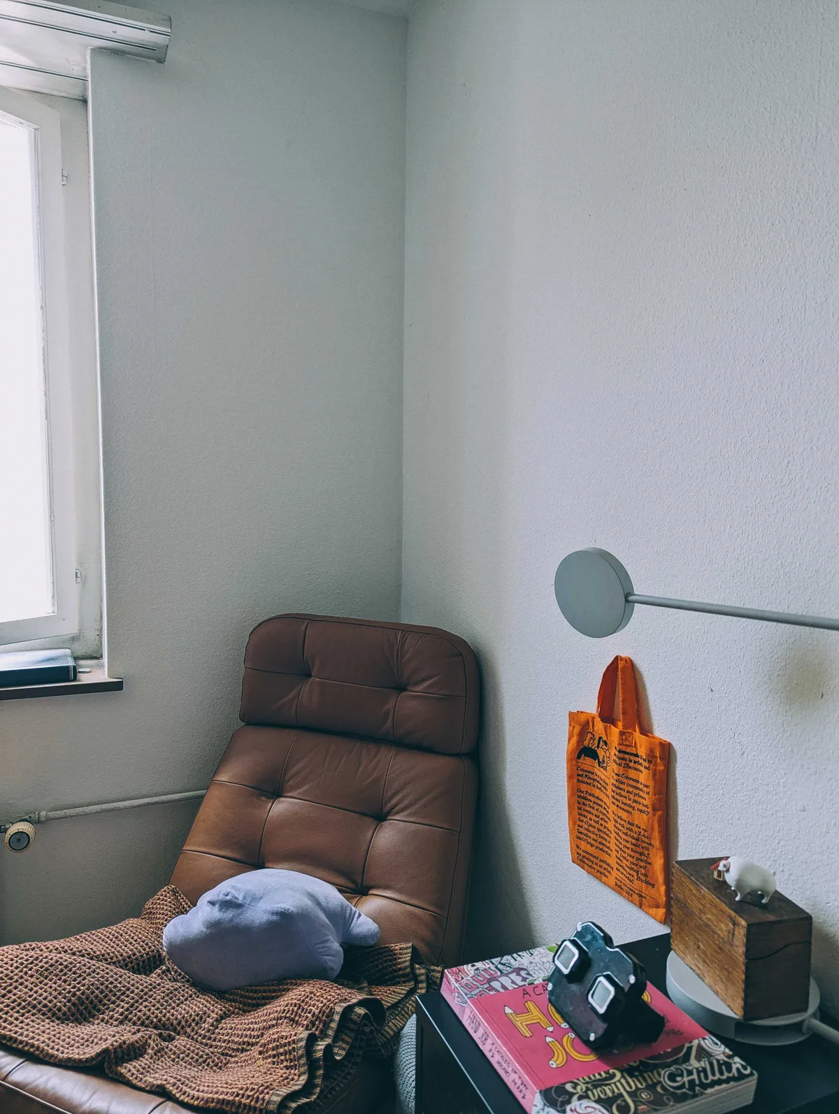 Reading nook with a brown leather recliner leaning against the corner of two empty white walls.