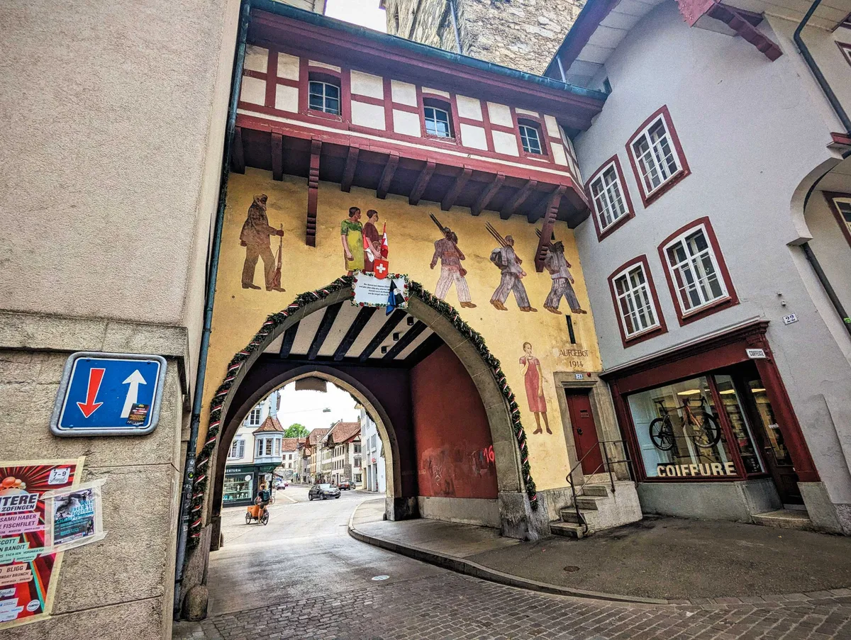 An archway with a mural depicting soldiers marching while the women look onwards.