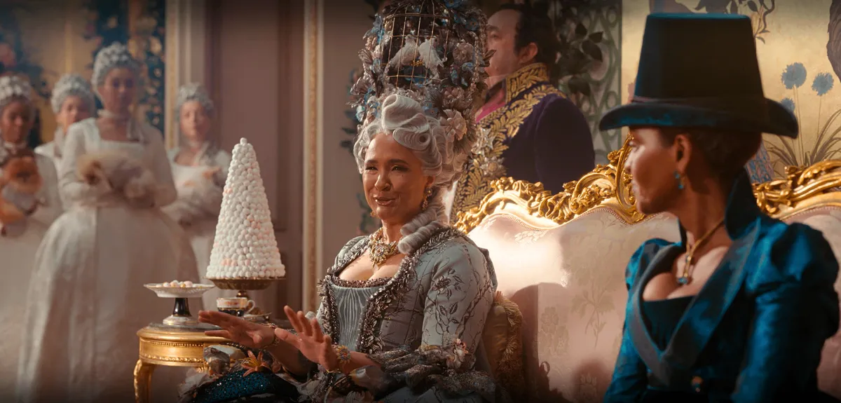Queen Charlotte wearing a tall wig that has an actual birdcage with two fake doves inside it.