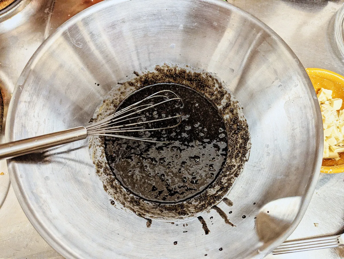 A silver mixing bowl is filled 1/4 with black liquid.