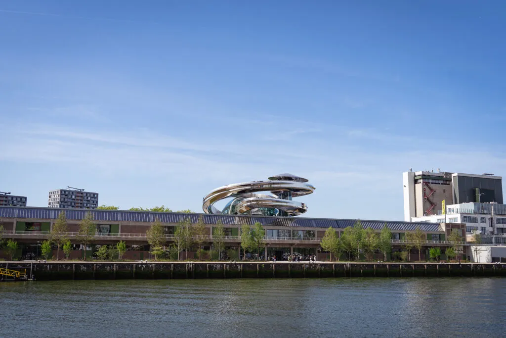 The museum overlooks the river. It is a long and flat warehouse building with a giant, metal spiral on the roof.