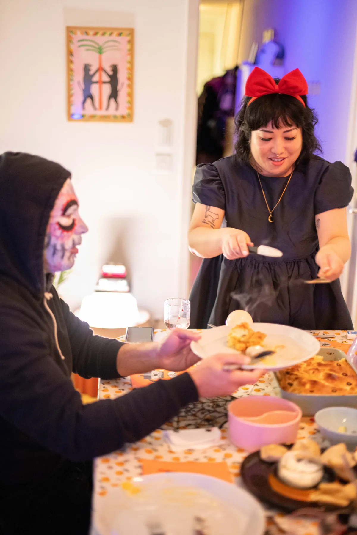 Peige dressed as Kiki the witch, serving pie to guests. Naim is on the left wearing dia de los muertos face paint.