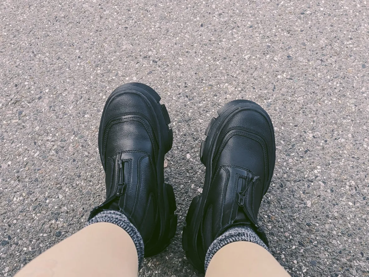 A pair of black boots with zips on the front. Peige's legs are cropped out and some grey socks are peaking out from the boots.