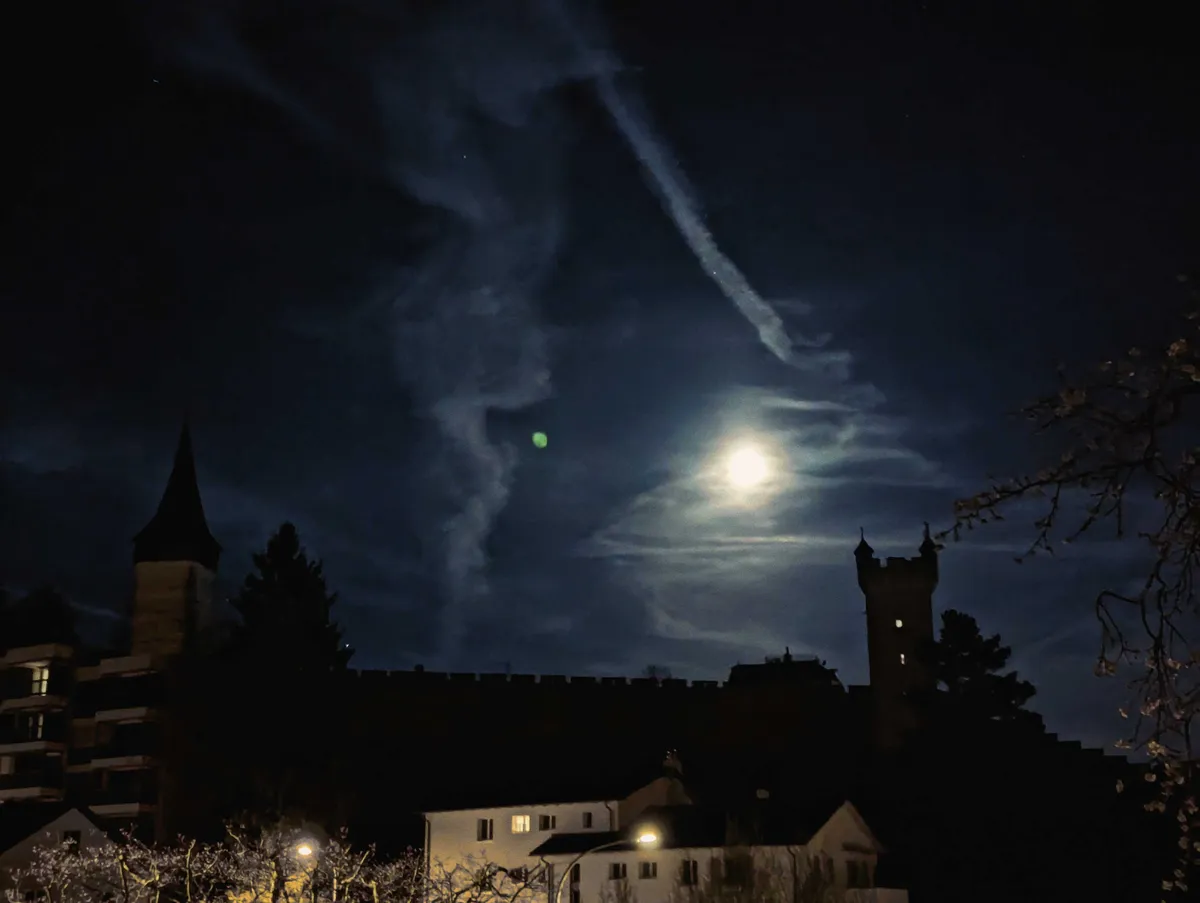 The silhouette of towers against a dark sky. The moon shines brightly, illuminating the clouds.