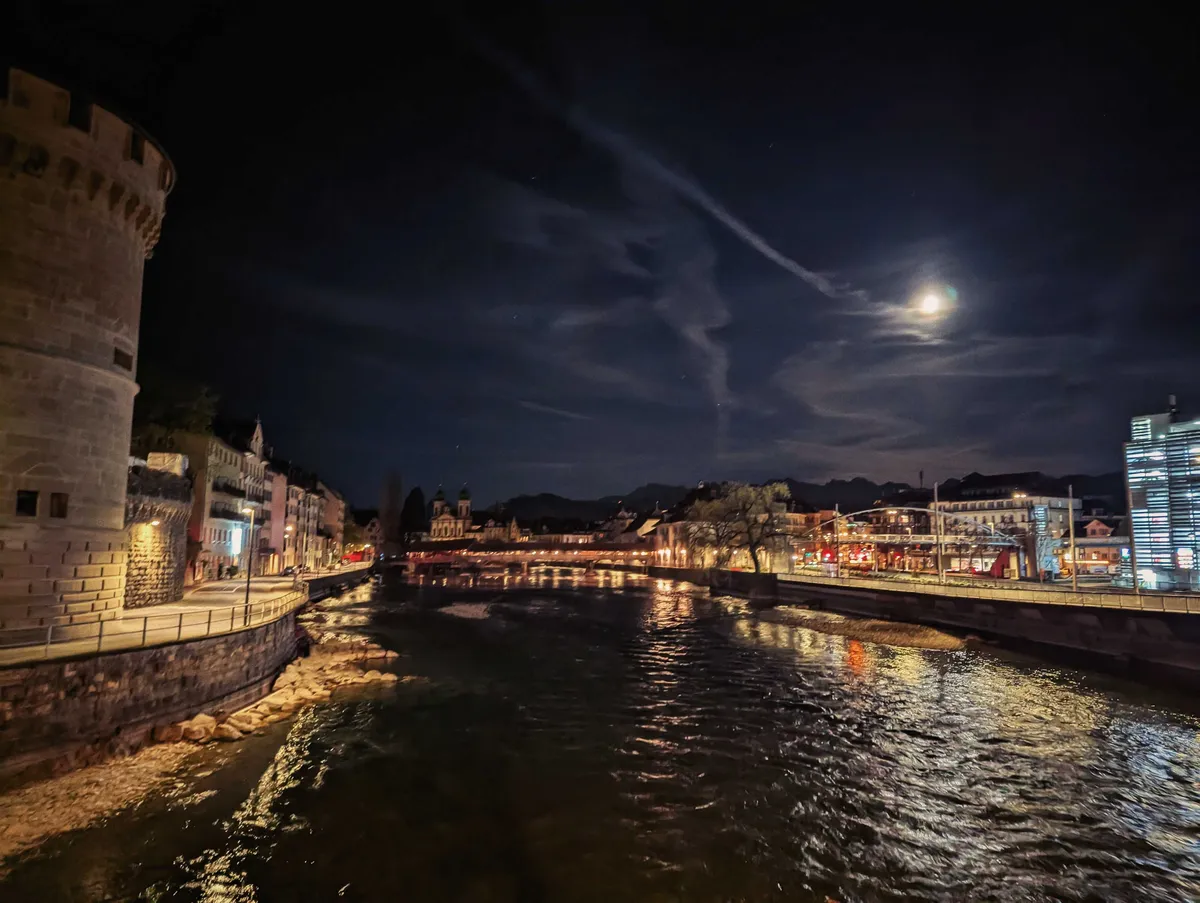 A view of the Reuss River in the moonlight night. The streets are sparkling with golden lights.