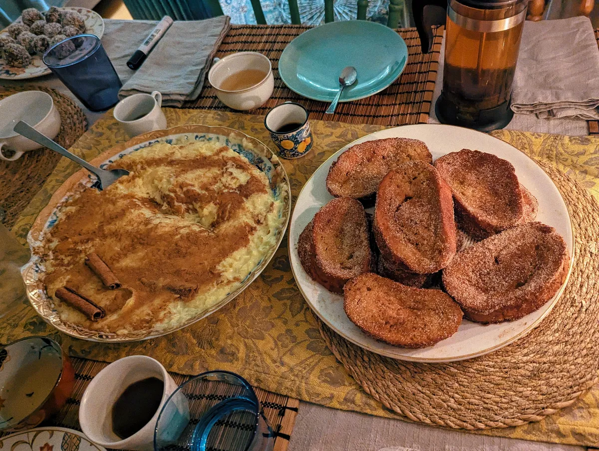 A plate of rice pudding with a generous amount of cinnamon sits next to a plate filled with sugared toast.