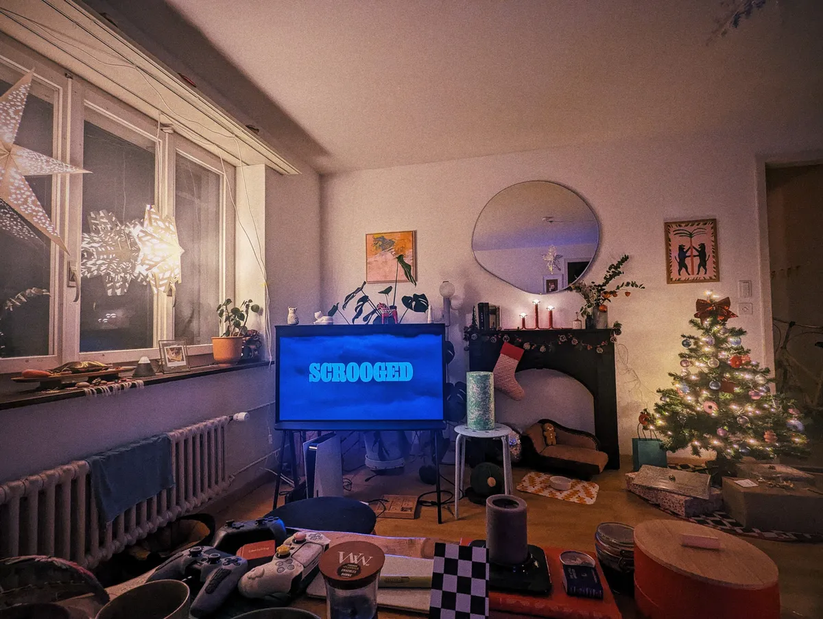 A cozy living room filled with lit, Christmas decor. The title image for the movie "Scrooged" is displayed on the TV.