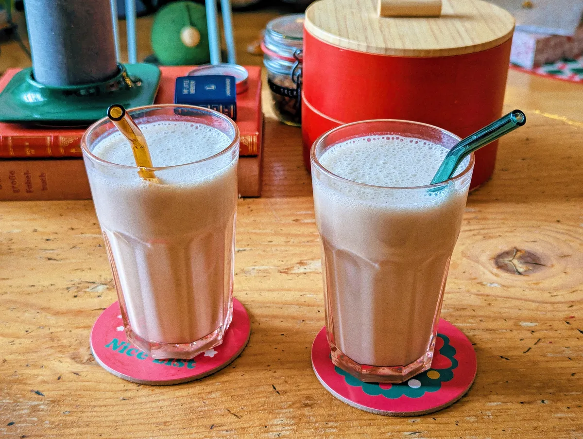 Two cups filled with banana milk are placed next to each other.