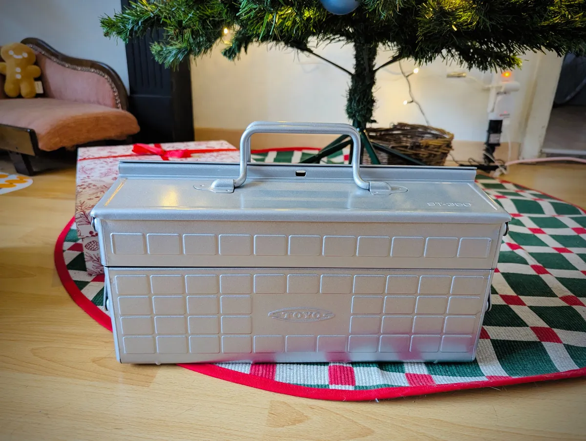 A silver metal toolbox is displayed at the foot of the Christmas tree.
