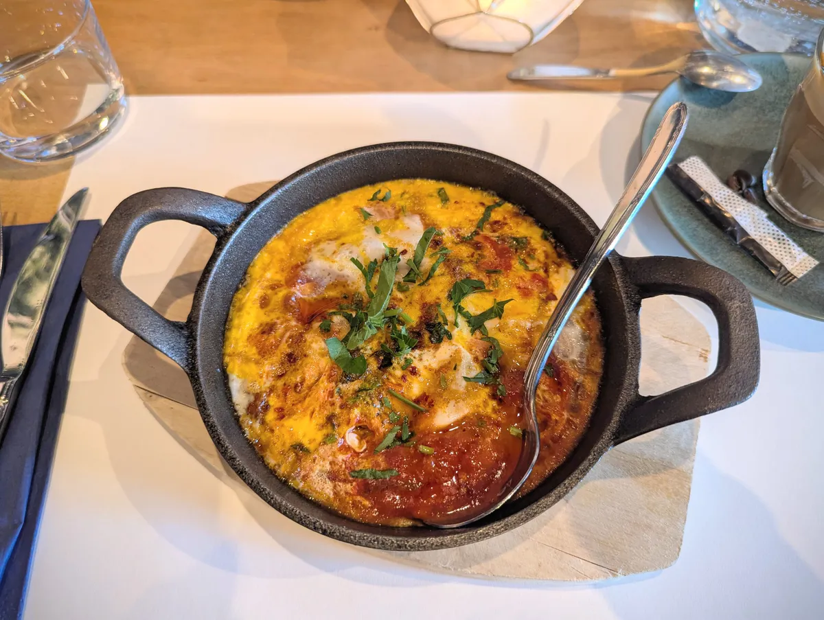 A mini cast iron pan filled with eggs cooked in saucy tomato.