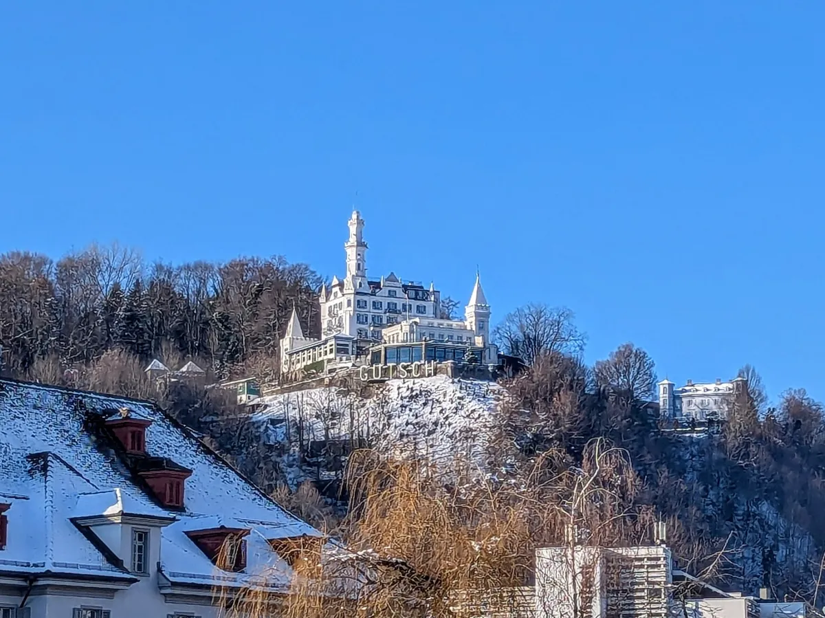 A sunny day with clear blue skies and a castle-like building with the letters spelling Gütsch seen on the hilltop.