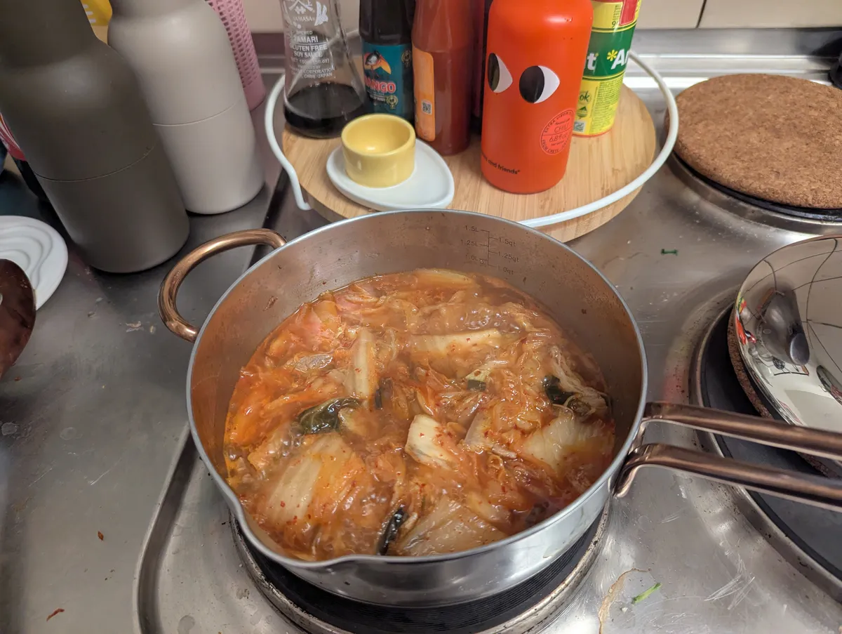 A silver pot filled with kimchi soup is boiling on the stove.