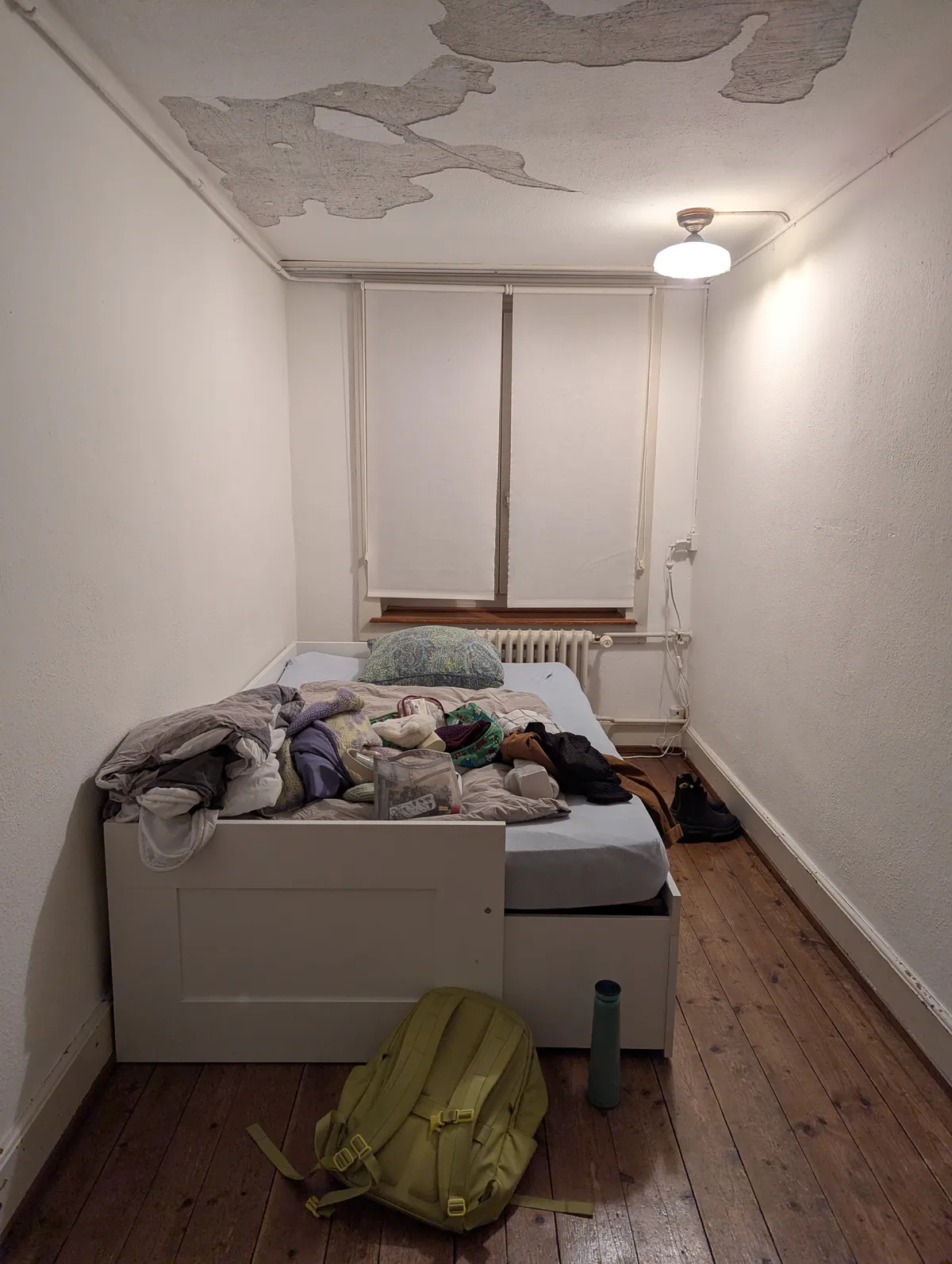 A small room with a bed that has a bunch of clothes and things on it.
