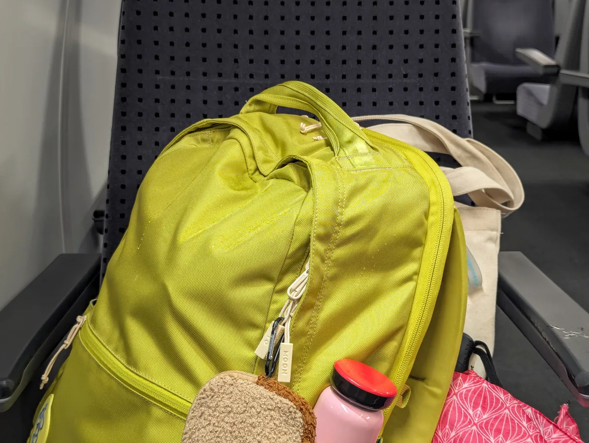 A bright pea green backpack on a train seat with a pink water bottle peeking out.