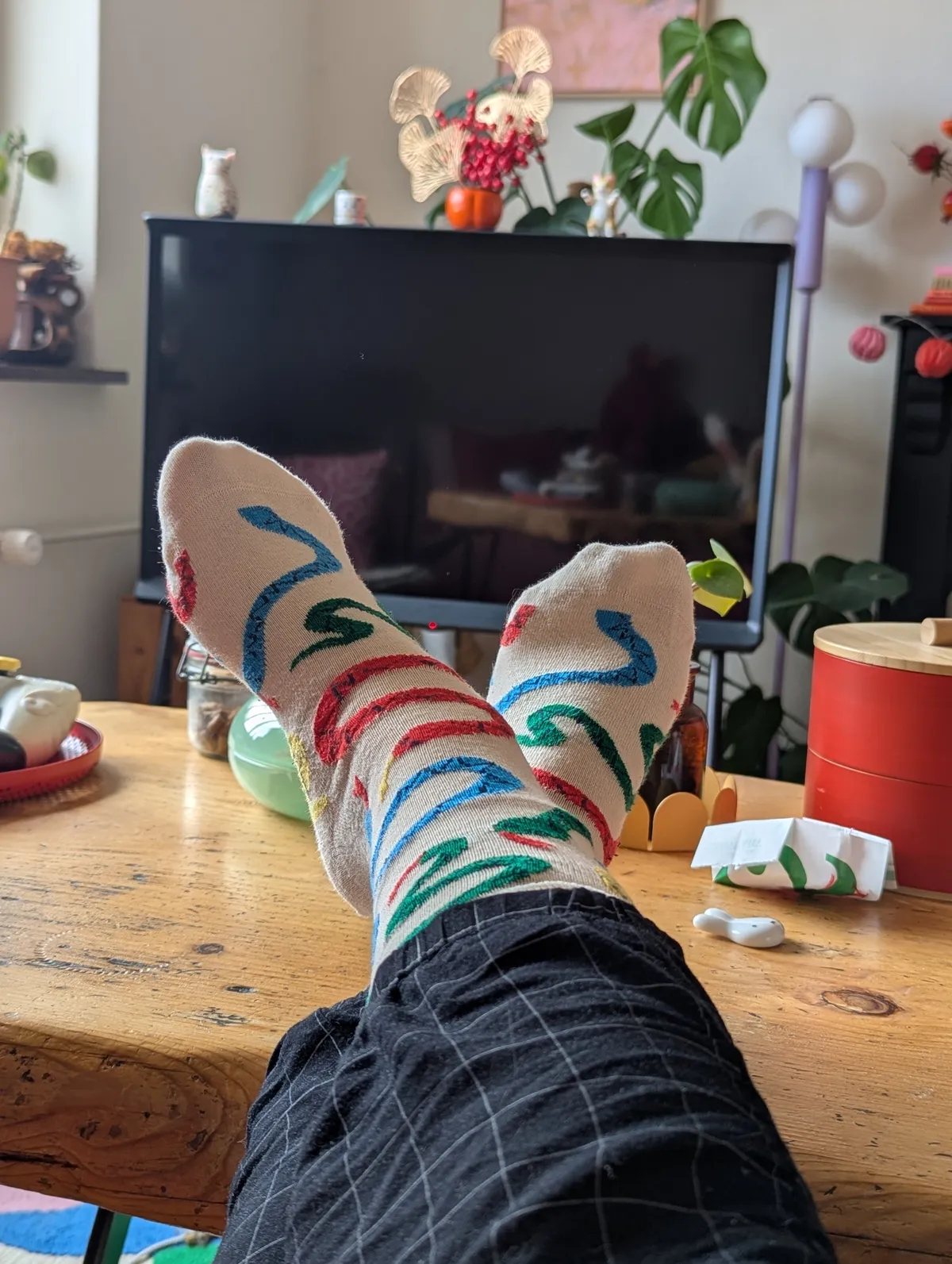 Peige wearing white socks with colorful snakes on them. Their feet are crossed and propped up on the coffee table.