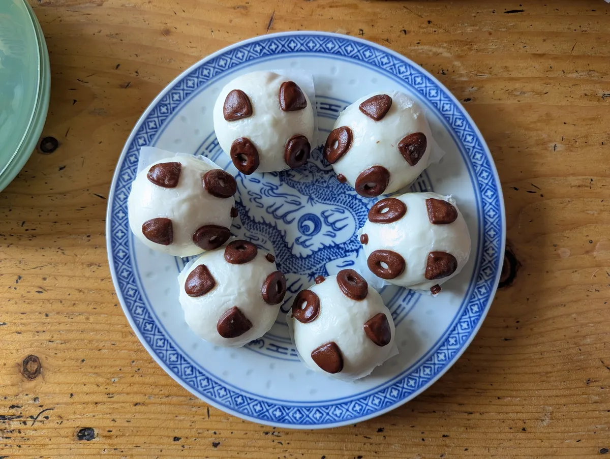 6 small buns decorated like pandas face each other in a circle on a white and blue ceramic plate.