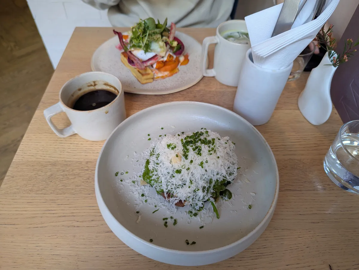 A plate with a slice of English muffin loaded generously with spinach, avocado, green sauce, finely shredded parmesan. And a cup of coffee.