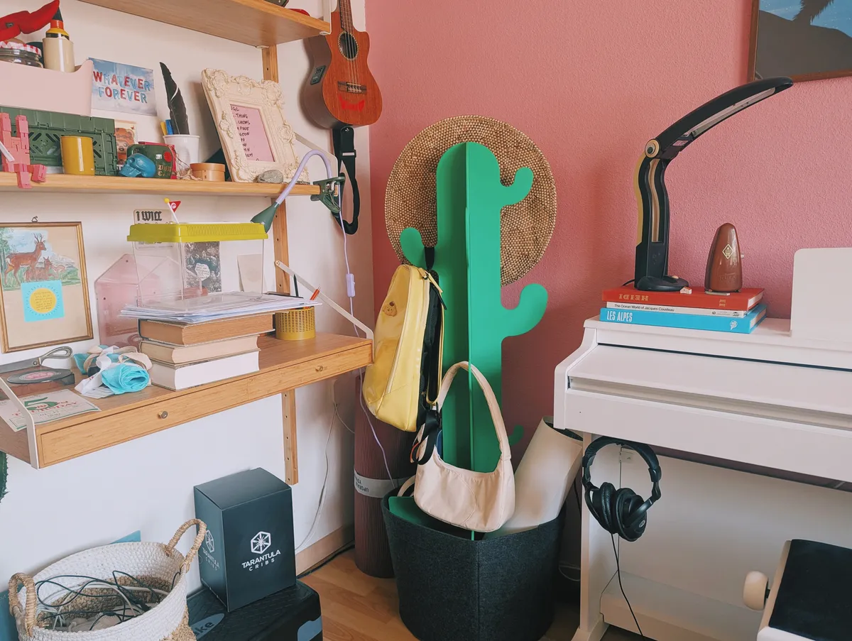 A cactus-shaped coat rack with things hanging from it. It stands in a corner next to the white piano.
