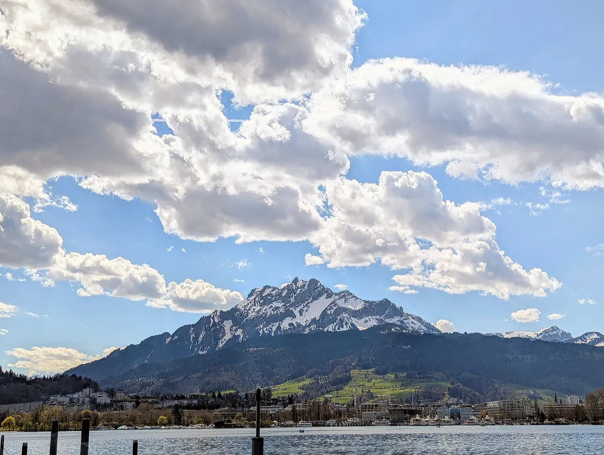Lakeside view of Mt. Pilatus with fluffy clouds against a blue sky.