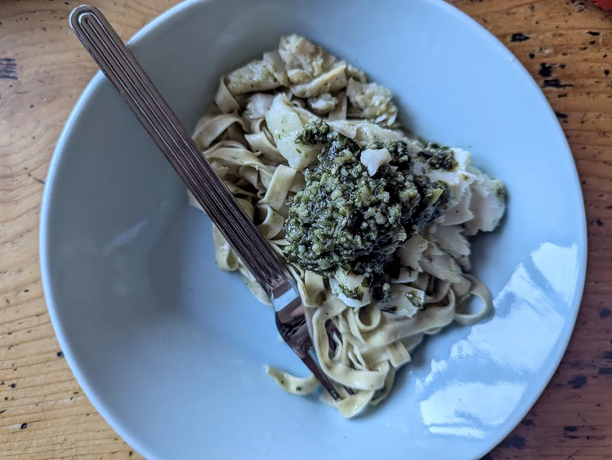 Tagliatelle with pesto and white fish on a light blue plate.