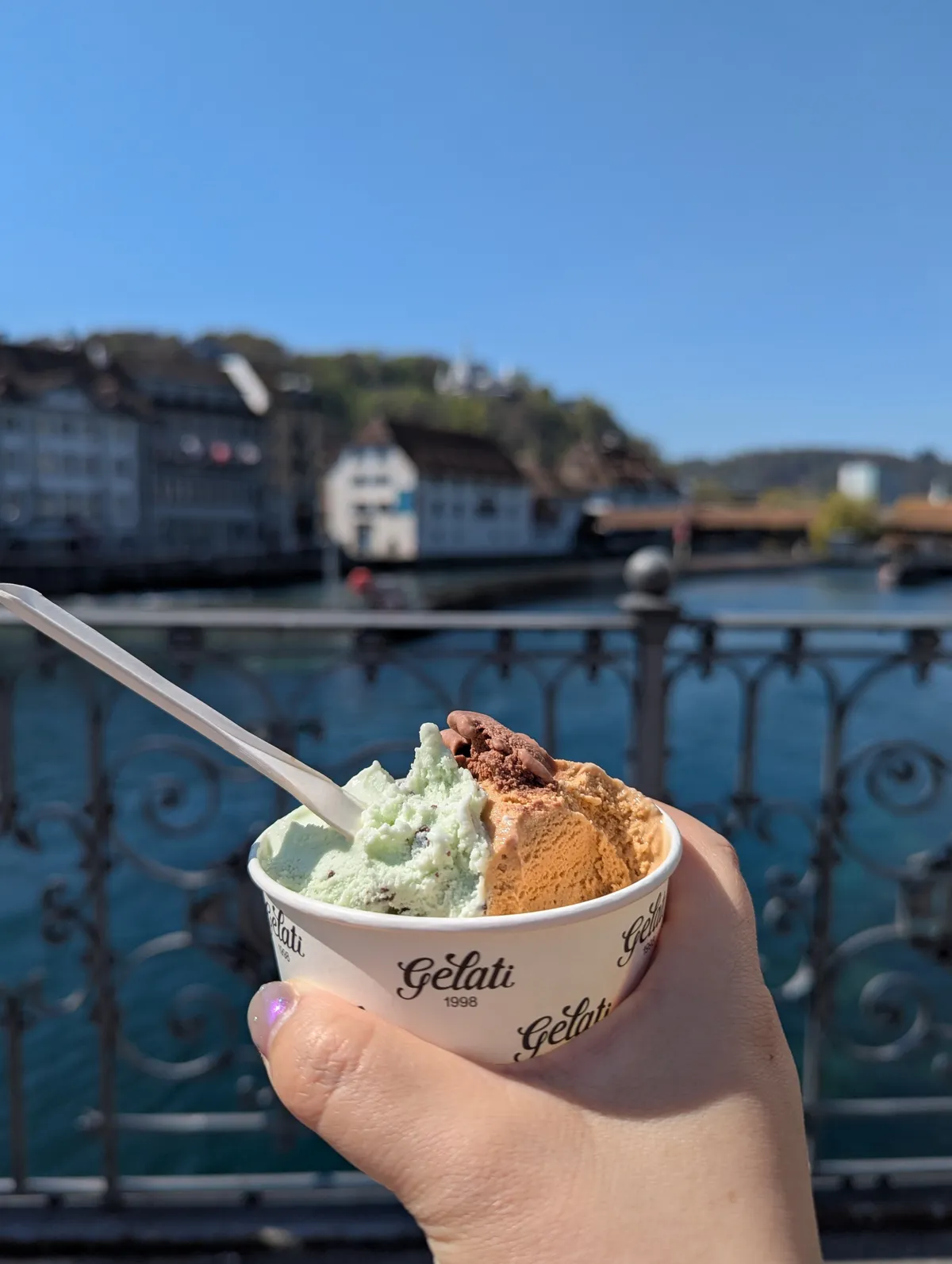 Peige holding a cup containing three flavors of ice cream in front of a bridge.