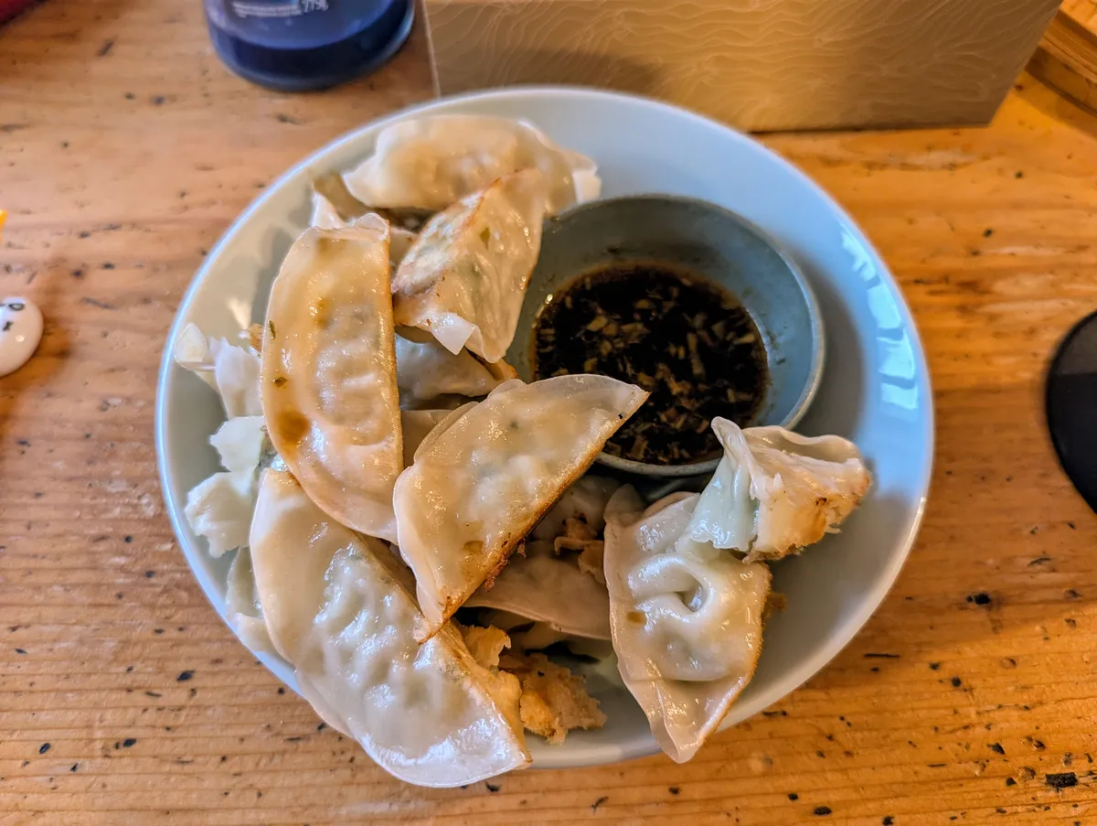 A plate of fried gyoza with soy sauce on the side.