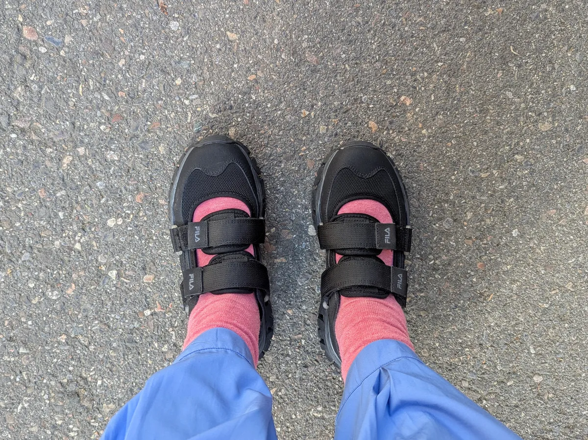 Peige wearing black Fila sneakers with two straps across the foot.