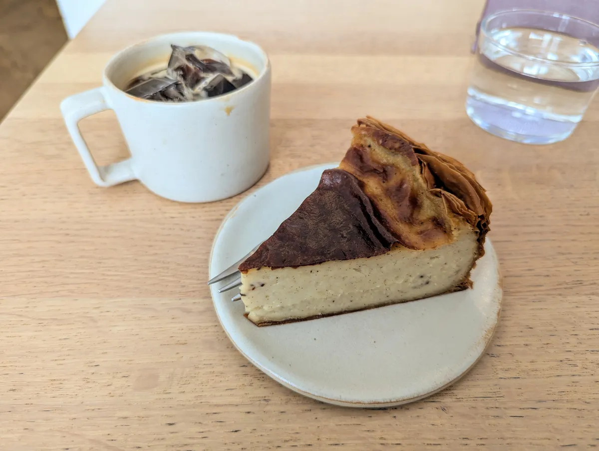 A slice of vanilla flan on a plate and an iced Americano in a small mug.