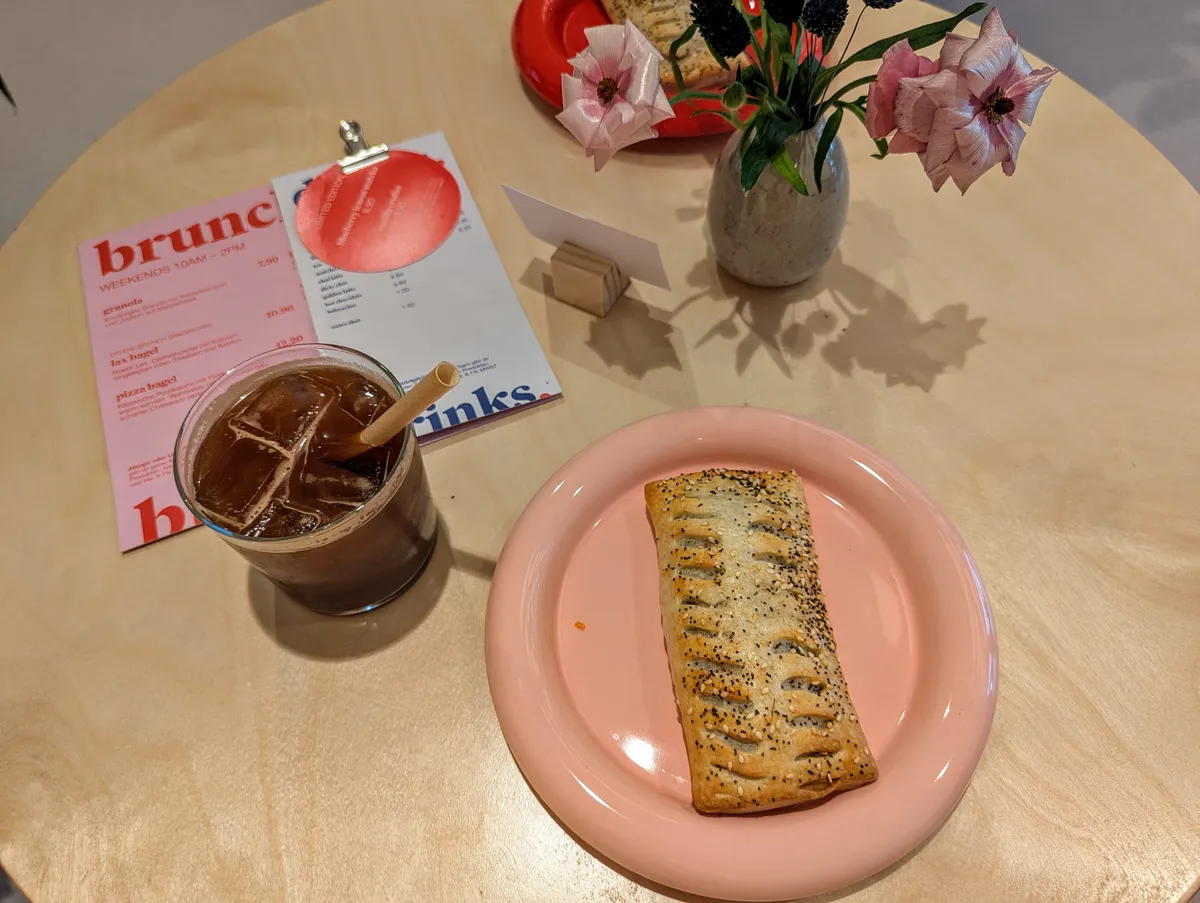 A stylish presentation of an iced Americano and a pastry on a pink plate.