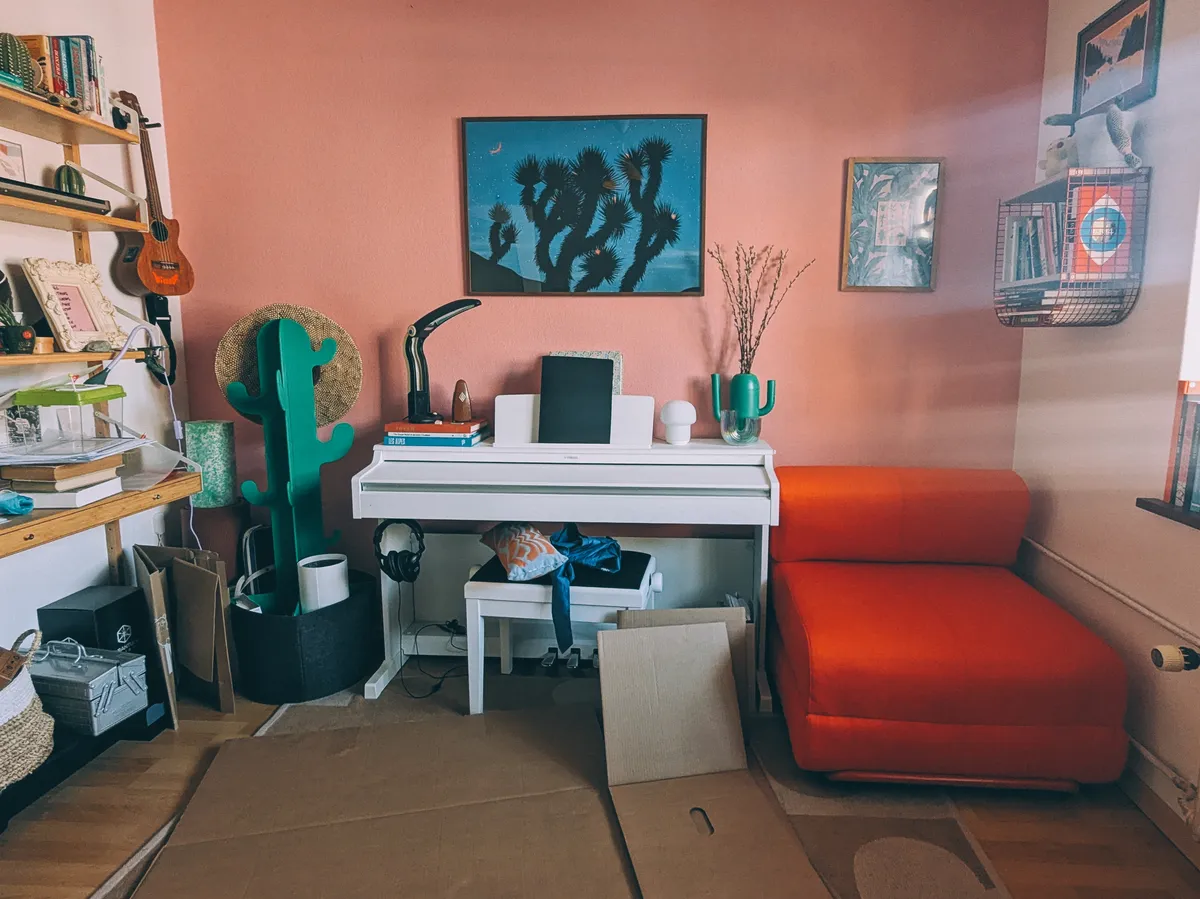 A red folding one-seater in the corner next to a white piano.