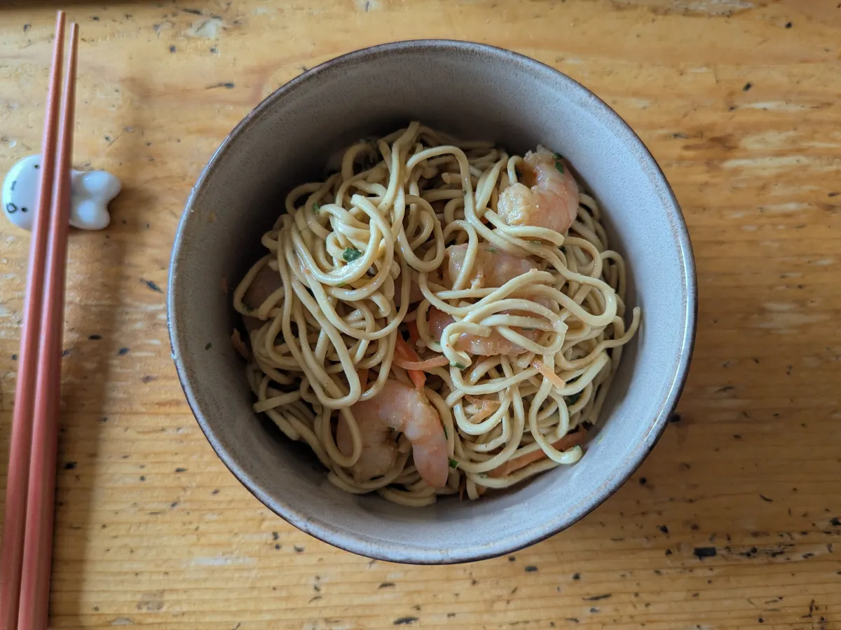 A bowl of noodles with shrimp, peanut sauce, chives, and carrots.