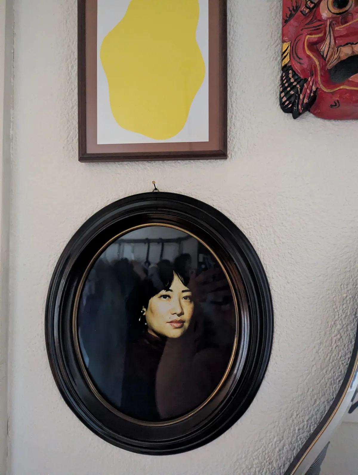 Peige smiling slightly in an oval frame. The portrait is high contrast with yellow-blue undertones.