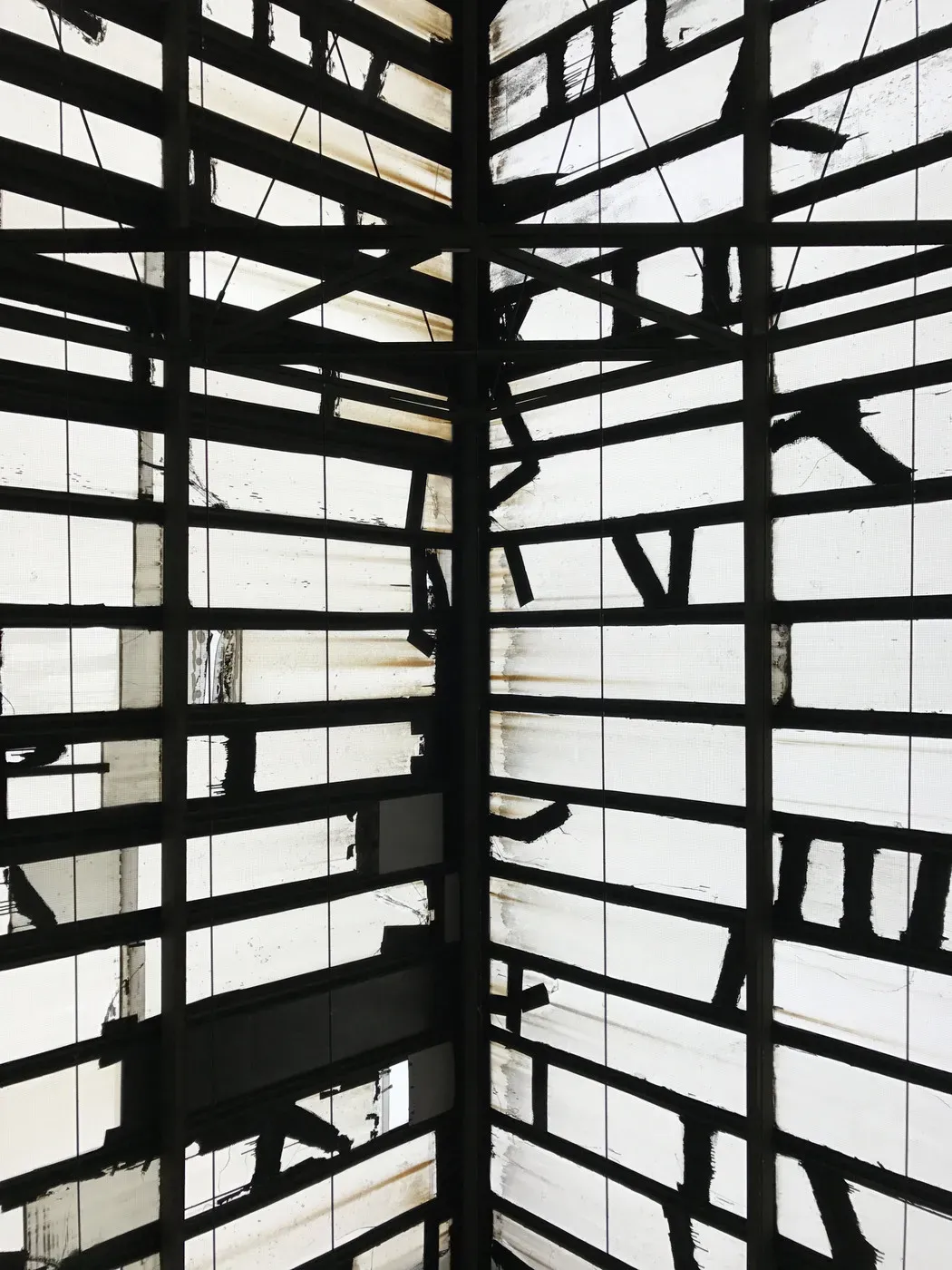 A geometric pattern of black and white lines fills the space, creating a fragmented, abstract design. The light filters through various panes, revealing shadows and textures that add depth to the structure.