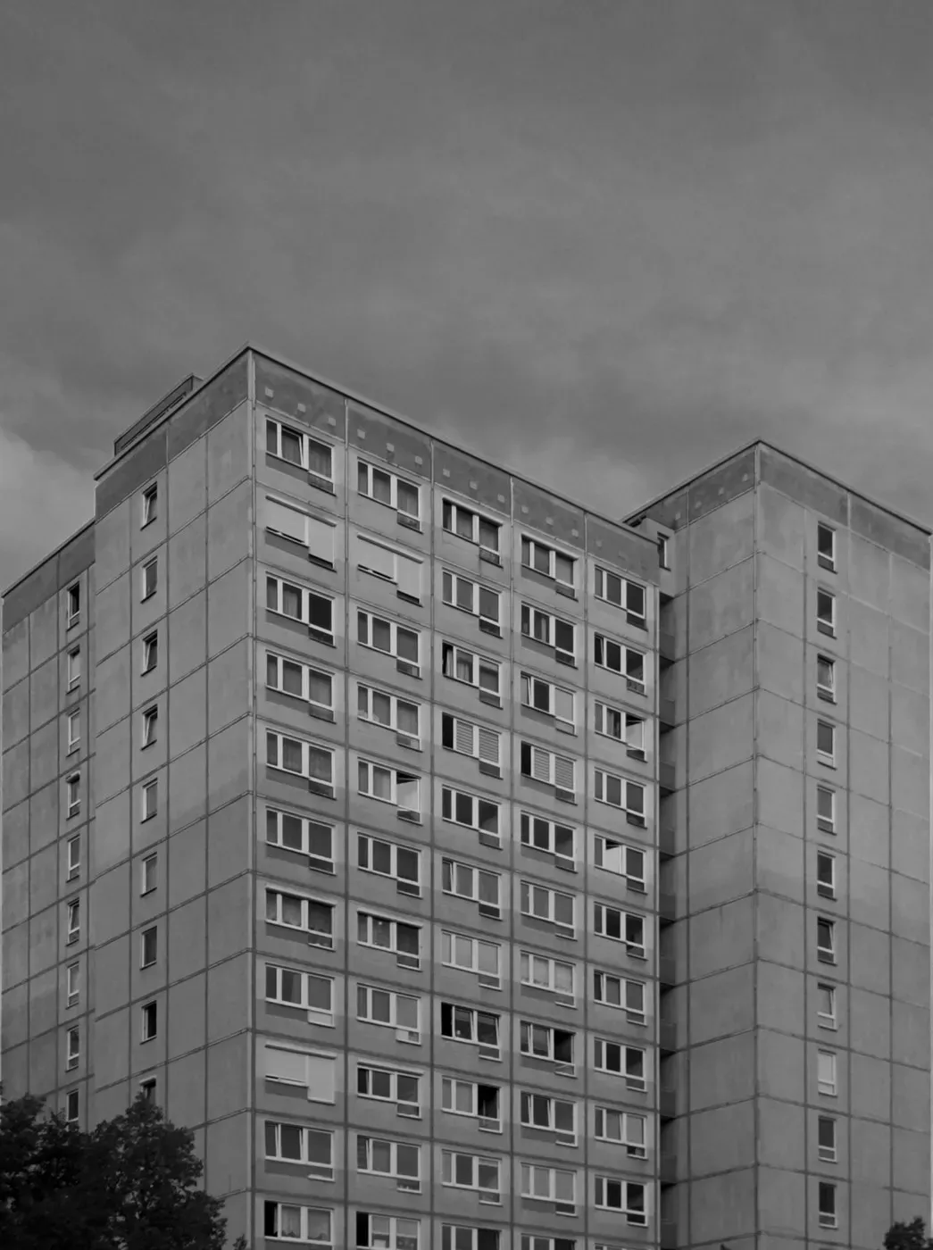 Tall residential building with a concrete façade, featuring multiple rows of windows. The sky above is overcast, adding a dramatic ambiance to the scene.