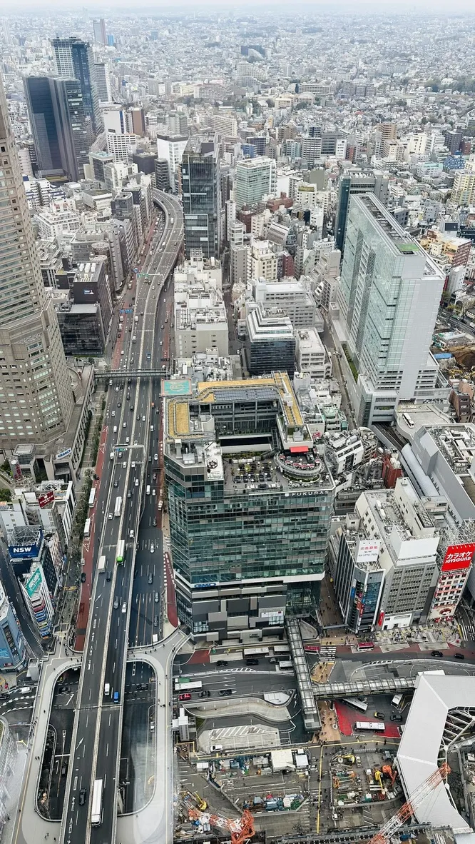 Aerial view of a sprawling urban landscape featuring a busy highway curving through the city, surrounded by a mix of modern high-rise buildings and various structures, with busy streets and intersections visible below.