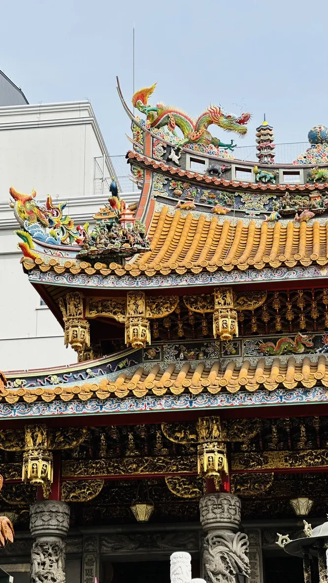 The image showcases an intricate and colorful traditional Asian temple roof, adorned with detailed carvings of dragons and mythical creatures. The ornate gold and vibrant hues of the tiles contrast with a clear blue sky in the background.